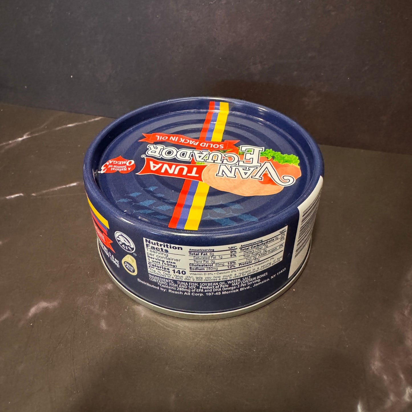 A can of Van Ecuador brand smoked tuna in oil with a blue lid, photographed on a dark gray countertop against a dark gray background.