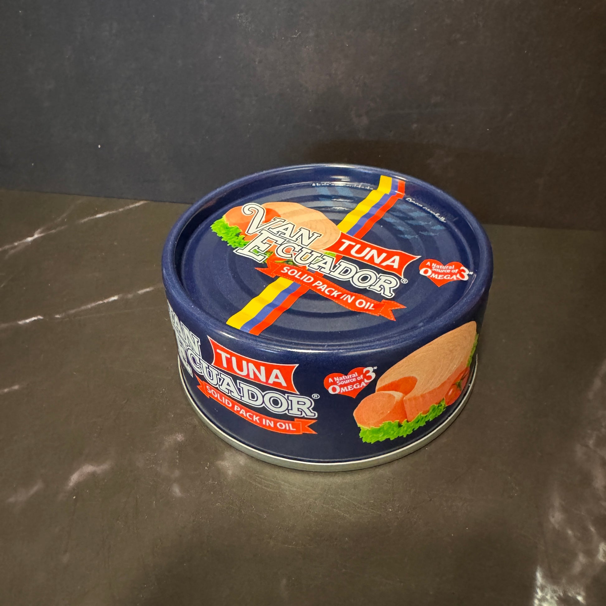 A can of Van Echtenad Tuna, solid pack in oil, with a dark blue label and colorful graphics, sitting on a dark gray marble-like surface.
